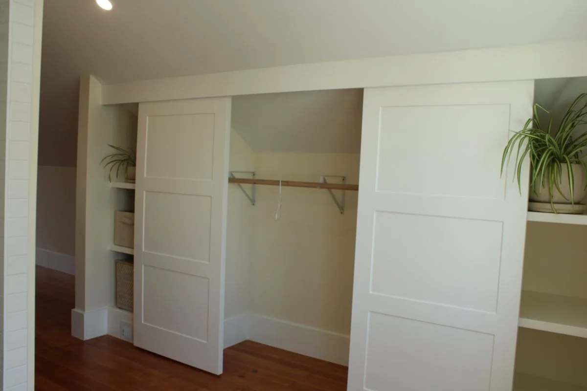 Custom white built-in bedroom closet with shaker style sliding doors and open shelving crafted by Buffalo Built LLC in Buffalo Wyoming.