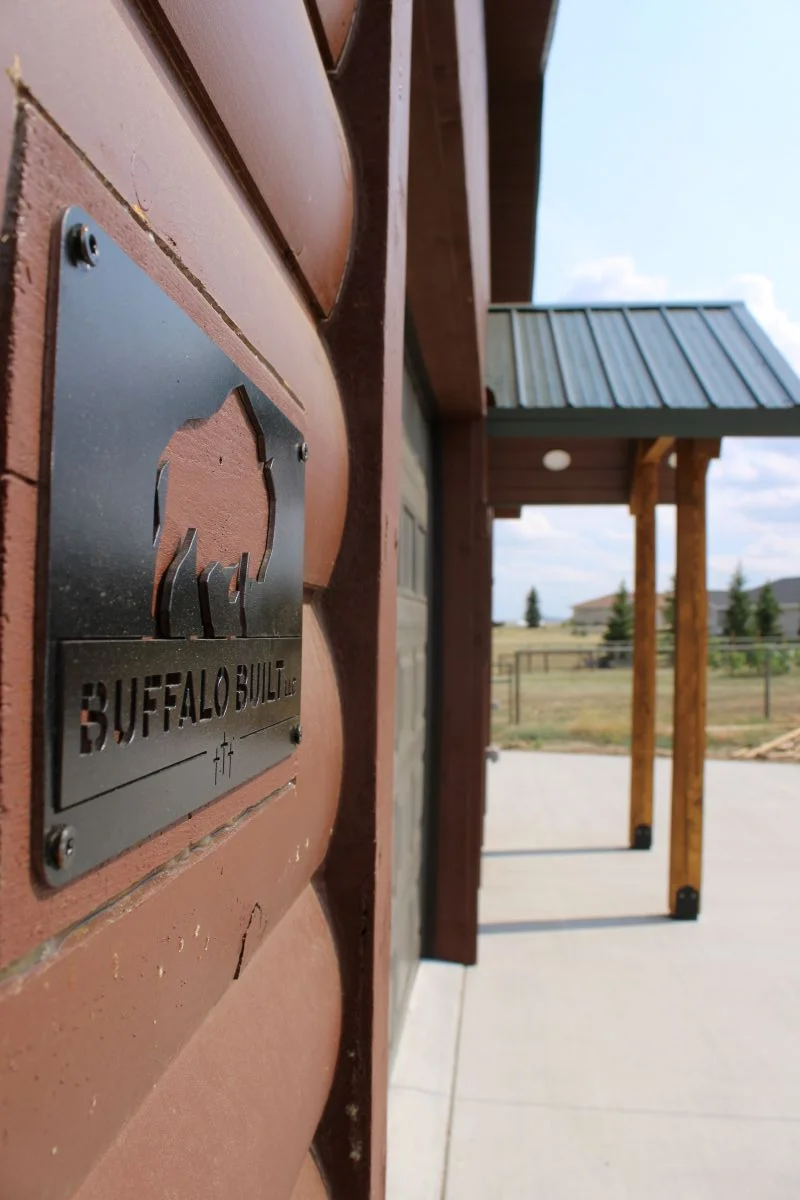 Custom metal Buffalo Built LLC company plaque mounted on log-lap siding of a completed commercial build in Wyoming.