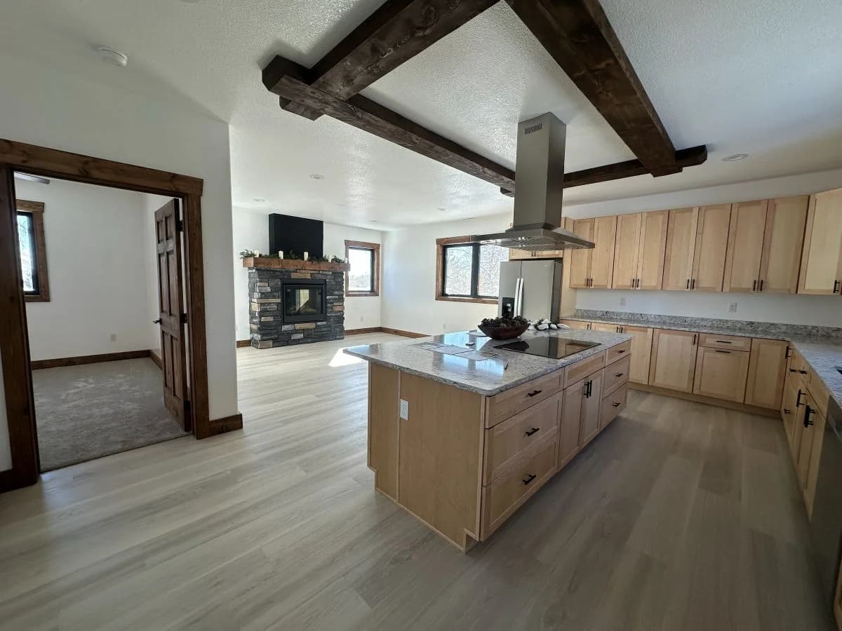 Luxury open concept kitchen and living area featuring custom light wood cabinets and a stone fireplace by Buffalo Built LLC in Buffalo, WY.