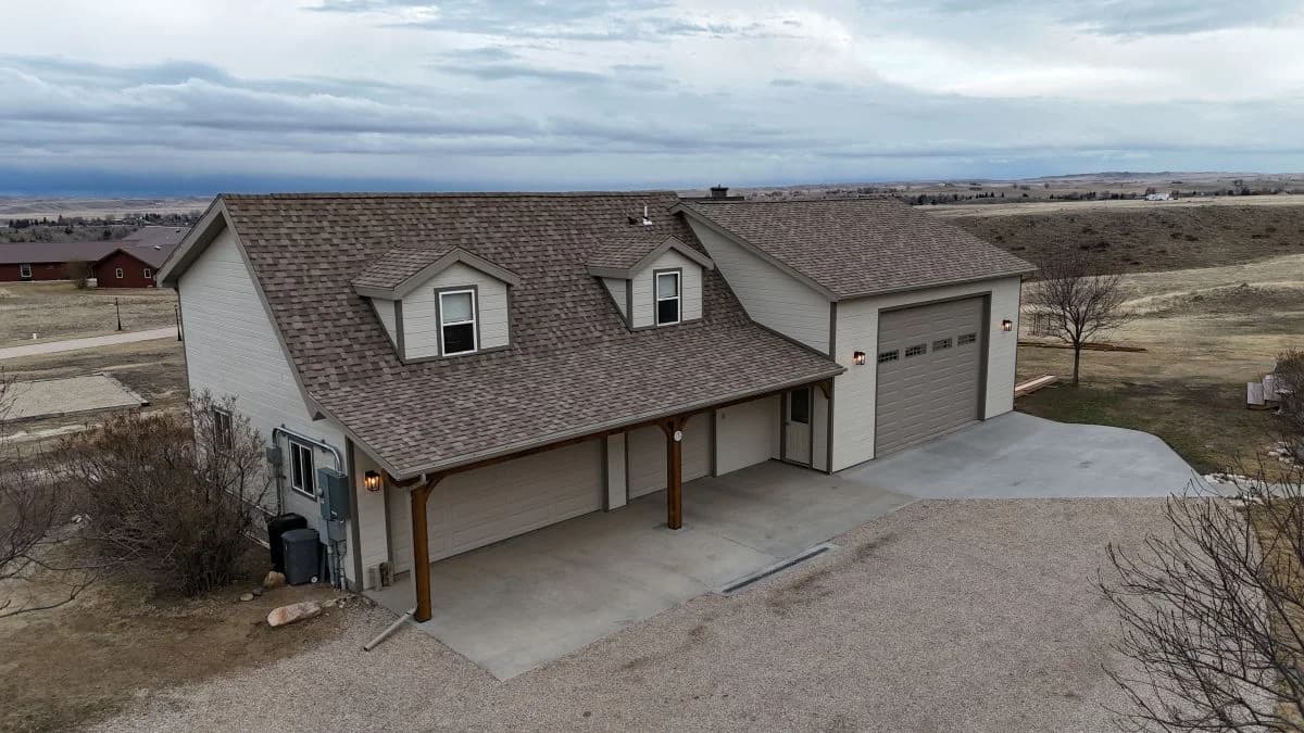 Completed multi-car garage addition showcasing tan vinyl siding, architectural roof shingles, dual dormer windows, and attached covered parking structure by Buffalo Built LLC in Buffalo Wyoming.