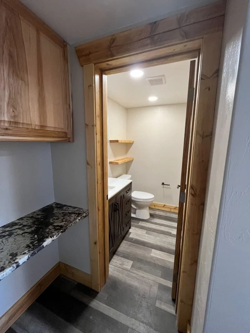 Modern bathroom remodel featuring a dark vanity, granite countertops, and natural wood door casing by Buffalo Built LLC.