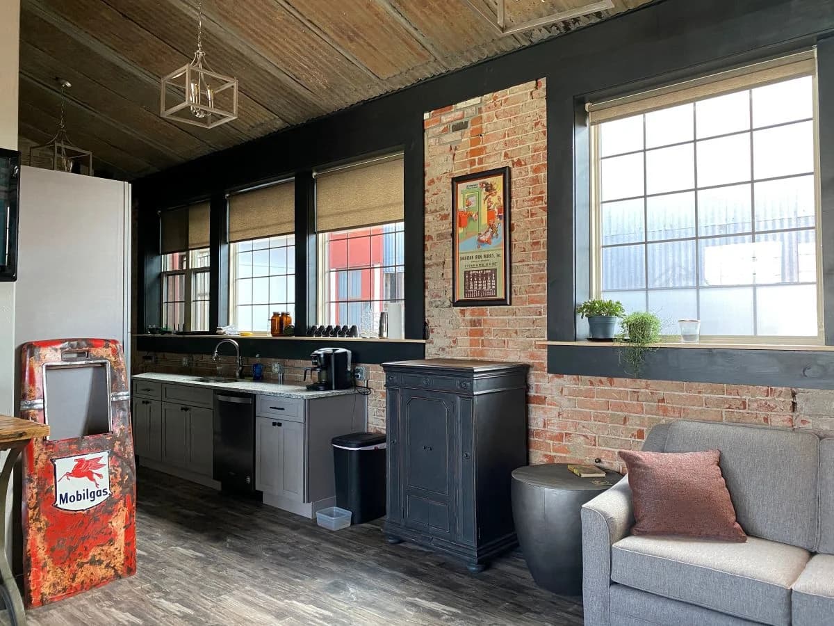 Open concept kitchen and living area renovation featuring custom grey cabinets, brick walls, and a vintage gas pump by Buffalo Built LLC.